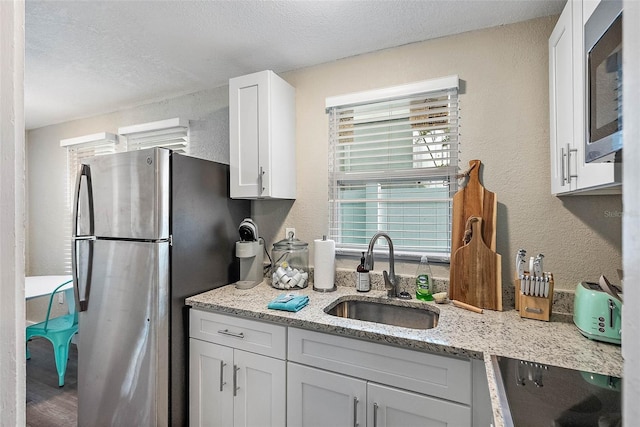 kitchen with light stone counters, white cabinetry, sink, and stainless steel appliances