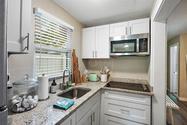 kitchen featuring black electric stovetop, sink, a textured ceiling, light stone counters, and white cabinetry