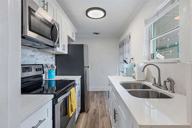 kitchen featuring sink, ornamental molding, appliances with stainless steel finishes, tasteful backsplash, and white cabinetry