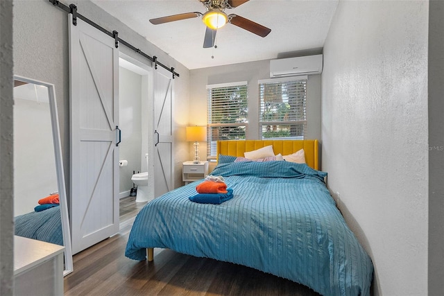 bedroom with connected bathroom, ceiling fan, a wall mounted air conditioner, a barn door, and hardwood / wood-style floors