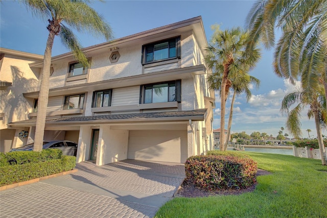 multi unit property with a water view, a front yard, stucco siding, decorative driveway, and a garage