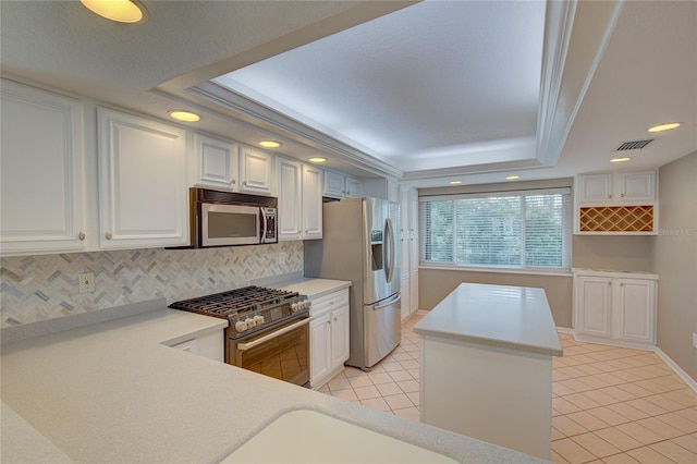 kitchen with tasteful backsplash, a tray ceiling, stainless steel appliances, ornamental molding, and white cabinets