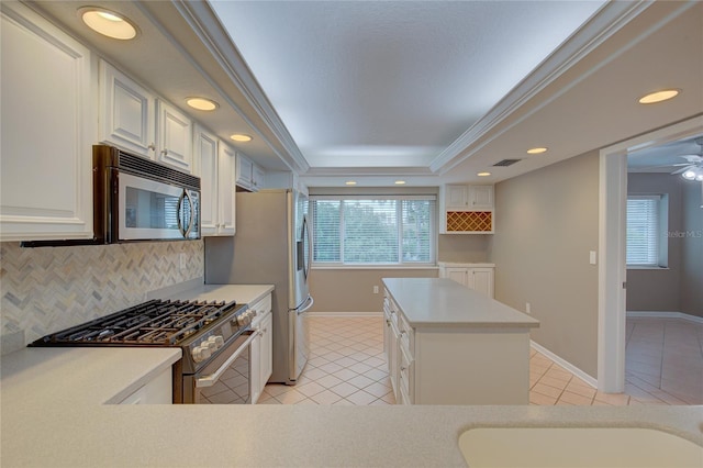 kitchen with white cabinetry, stainless steel appliances, decorative backsplash, a tray ceiling, and light tile patterned flooring