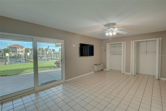 unfurnished bedroom with ceiling fan, an AC wall unit, access to exterior, two closets, and a water view