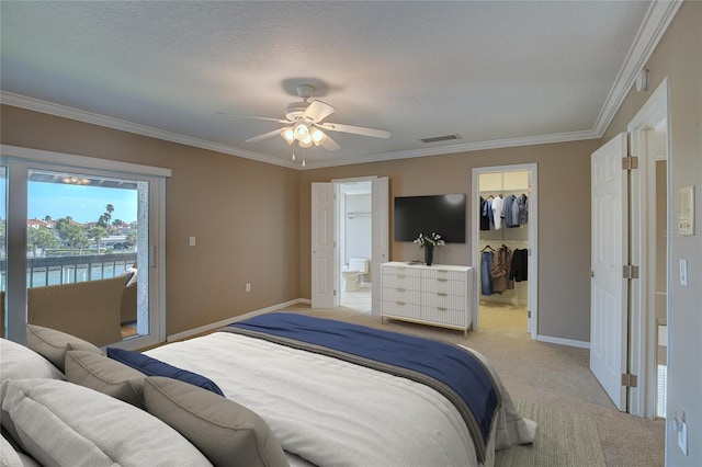 bedroom with a walk in closet, light colored carpet, visible vents, and ornamental molding