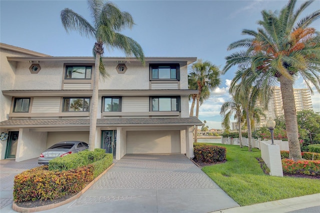 view of front of house featuring stucco siding, an attached garage, decorative driveway, and a front lawn