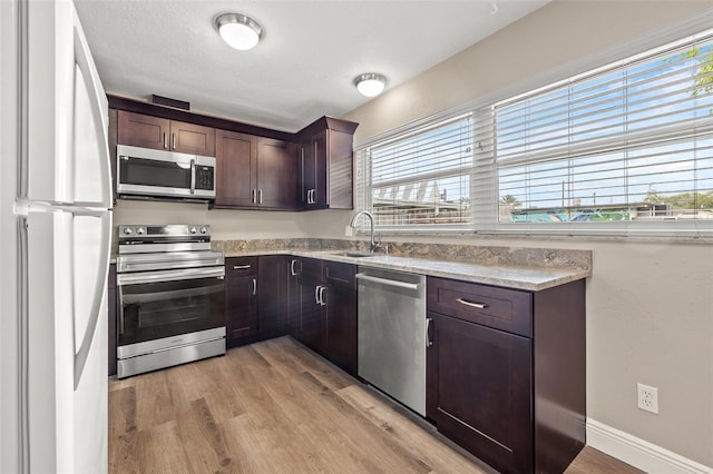 kitchen featuring appliances with stainless steel finishes, sink, light stone counters, dark brown cabinetry, and light hardwood / wood-style flooring