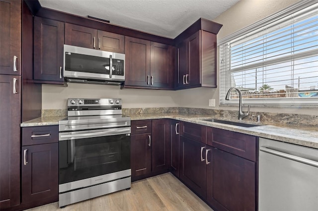 kitchen with sink, light hardwood / wood-style flooring, stainless steel appliances, light stone counters, and a textured ceiling