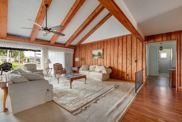 living room with ceiling fan, beamed ceiling, wood walls, wood-type flooring, and a textured ceiling