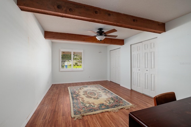 bedroom with a textured ceiling, ceiling fan, wood-type flooring, beamed ceiling, and multiple closets