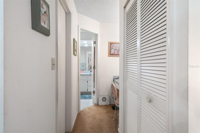 corridor with light colored carpet and a textured ceiling