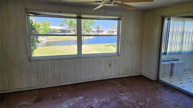 unfurnished room featuring ceiling fan, wood walls, a water view, and a healthy amount of sunlight