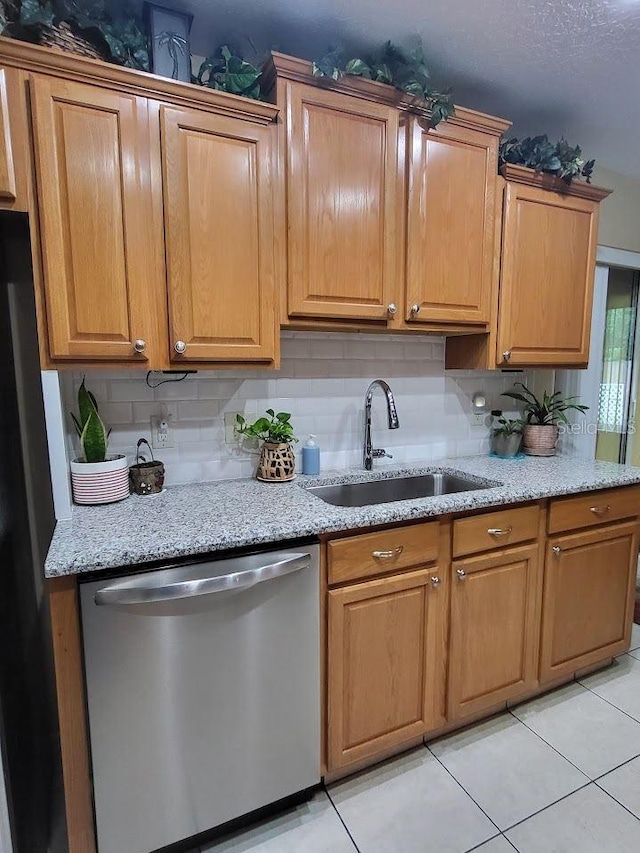 kitchen with decorative backsplash, light tile patterned flooring, light stone countertops, stainless steel dishwasher, and sink