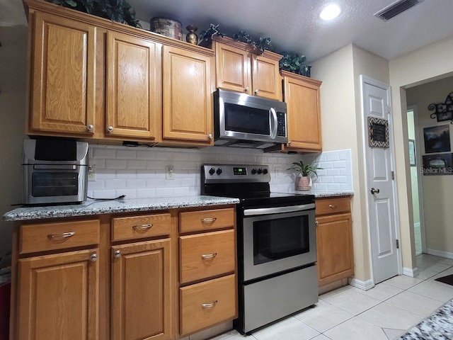 kitchen with stainless steel appliances, light stone counters, light tile patterned floors, and tasteful backsplash