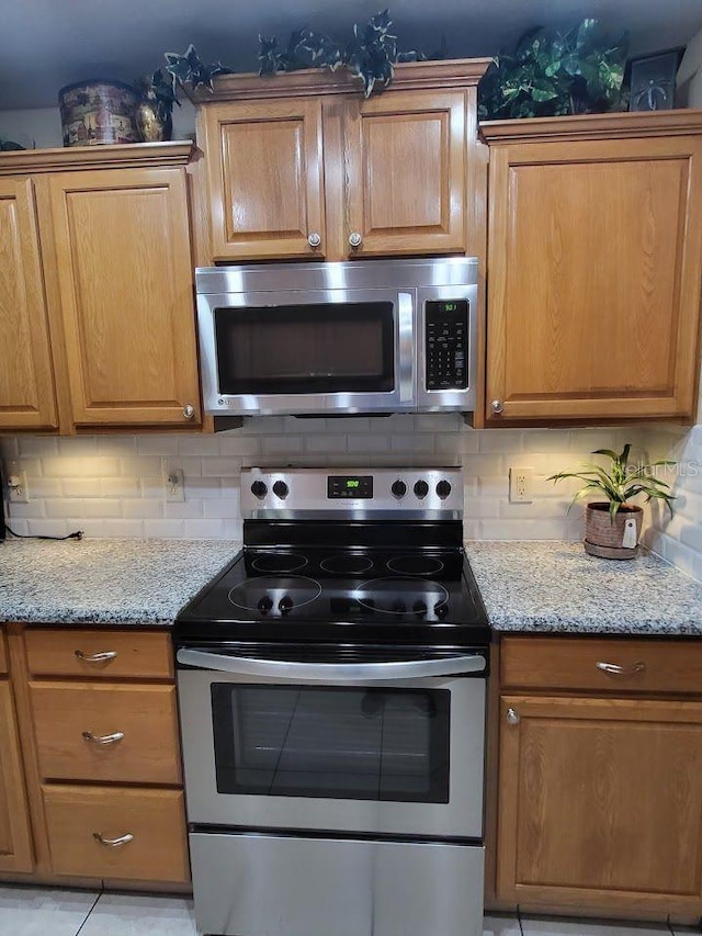 kitchen featuring light stone counters, light tile patterned floors, appliances with stainless steel finishes, and tasteful backsplash