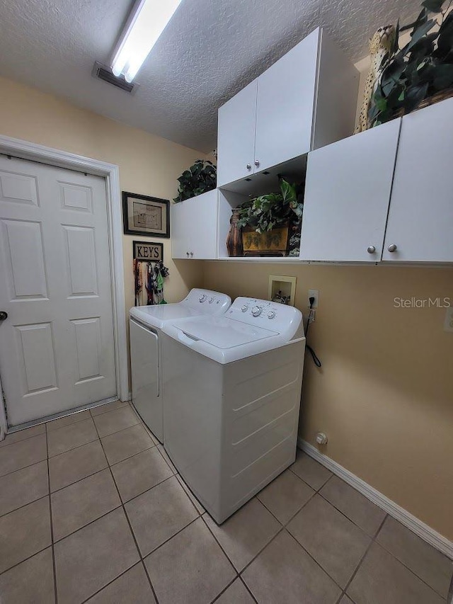 washroom featuring cabinets, a textured ceiling, light tile patterned floors, and washing machine and dryer