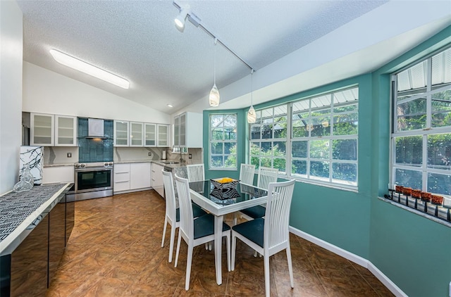 kitchen featuring hanging light fixtures, wall chimney range hood, oven, vaulted ceiling, and white cabinets