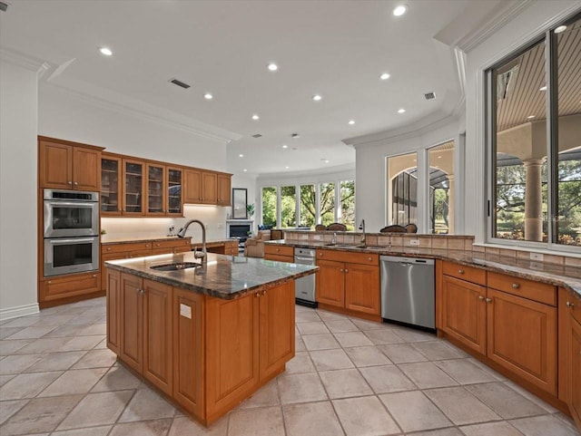 kitchen featuring a kitchen island with sink, dark stone counters, crown molding, sink, and appliances with stainless steel finishes