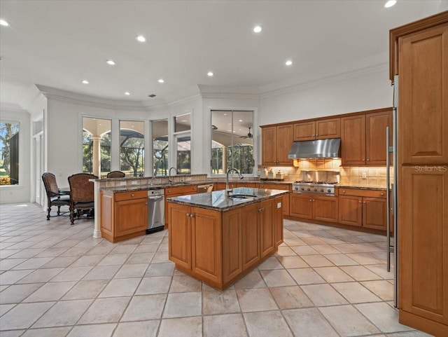 kitchen featuring sink, a healthy amount of sunlight, stainless steel gas cooktop, dark stone counters, and a kitchen island with sink