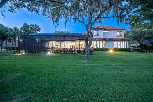 back house at dusk with a lanai and a yard