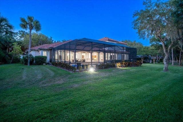 back house at dusk featuring a lawn and glass enclosure