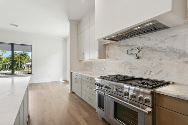 kitchen with range with two ovens, visible vents, backsplash, light wood finished floors, and custom range hood