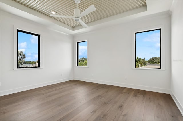 spare room featuring a ceiling fan, a tray ceiling, baseboards, and wood finished floors