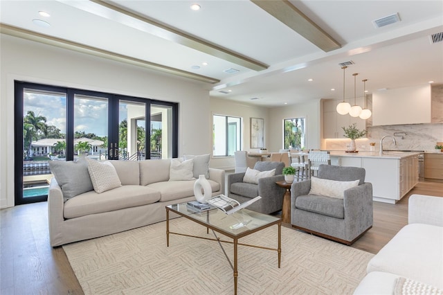 living room with french doors, beam ceiling, and light hardwood / wood-style floors