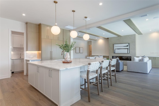 kitchen with light stone counters, a spacious island, beam ceiling, light wood-style flooring, and backsplash