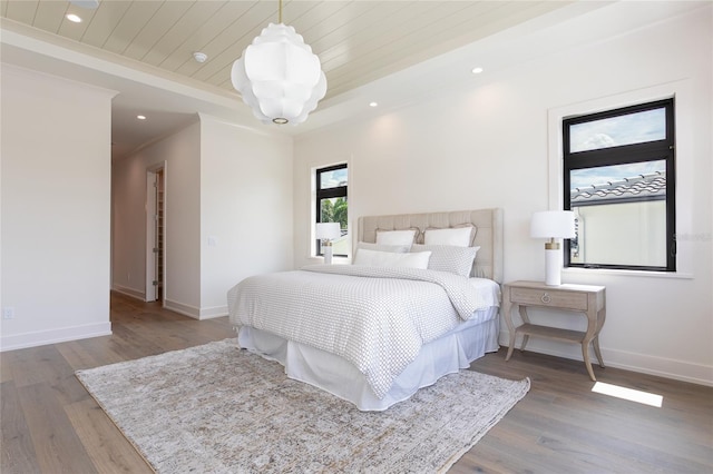 bedroom with a tray ceiling, recessed lighting, wood finished floors, and baseboards