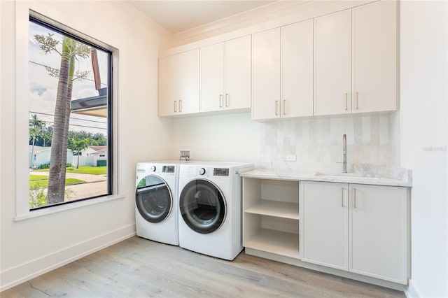 clothes washing area with light wood-type flooring, sink, washer and dryer, cabinets, and ornamental molding