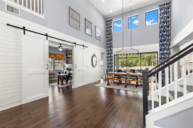 entryway featuring ceiling fan, a barn door, dark hardwood / wood-style flooring, and a high ceiling