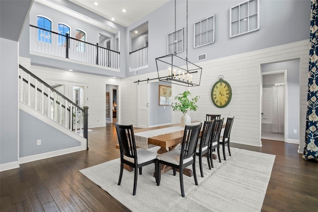 dining area featuring dark hardwood / wood-style floors, a barn door, a high ceiling, and an inviting chandelier