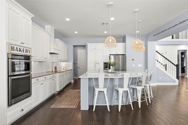 kitchen with white cabinets, pendant lighting, stainless steel appliances, and an island with sink