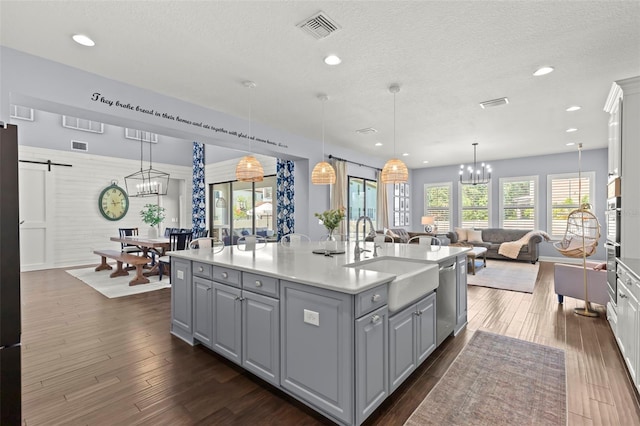 kitchen with sink, a barn door, stainless steel dishwasher, an island with sink, and decorative light fixtures