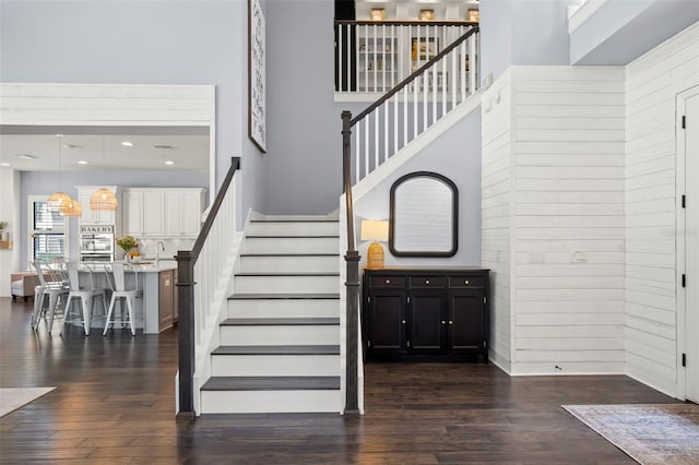 stairs with a high ceiling, hardwood / wood-style flooring, wood walls, and sink