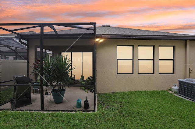 back house at dusk featuring glass enclosure, a patio area, a yard, and central AC