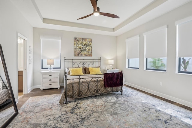 bedroom featuring ensuite bathroom, a tray ceiling, wood finished floors, and baseboards