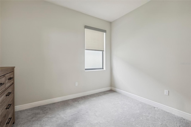 spare room with baseboards and light colored carpet