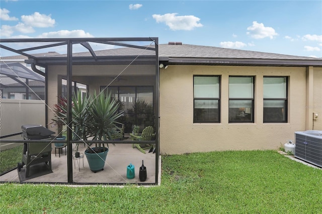 back of property featuring glass enclosure, cooling unit, a shingled roof, a lawn, and stucco siding