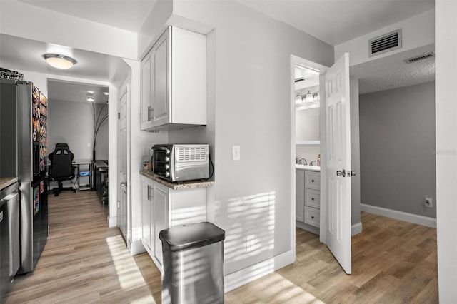 kitchen with white cabinets, stainless steel fridge, stone countertops, and light hardwood / wood-style flooring