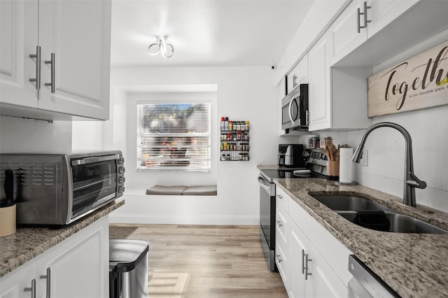 kitchen featuring white cabinets, appliances with stainless steel finishes, light stone countertops, and sink