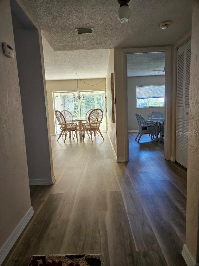 hall featuring wood-type flooring, a textured ceiling, an inviting chandelier, and a wealth of natural light