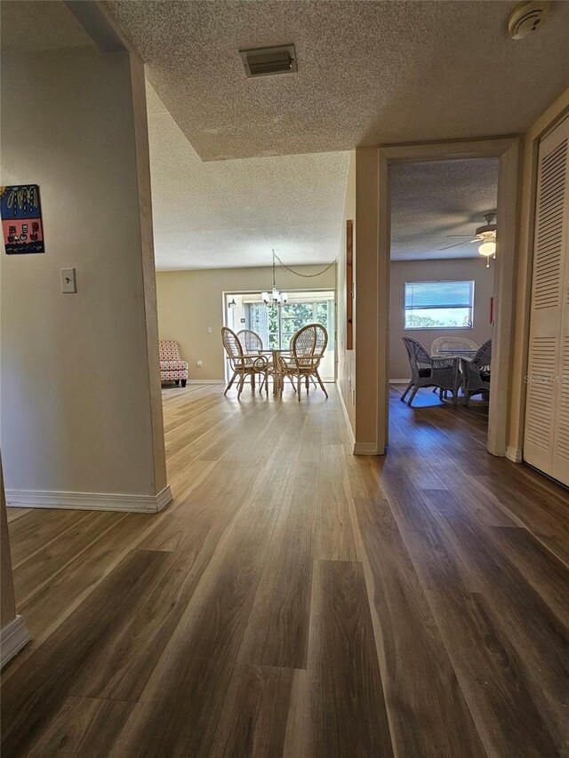 hall with hardwood / wood-style floors, a textured ceiling, and a notable chandelier