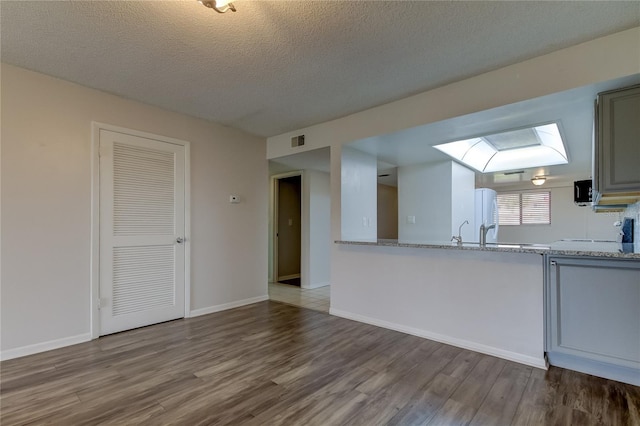 kitchen featuring a skylight, sink, light stone counters, wood-type flooring, and a textured ceiling