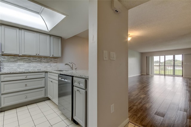 kitchen featuring decorative backsplash, light stone countertops, stainless steel dishwasher, sink, and gray cabinets