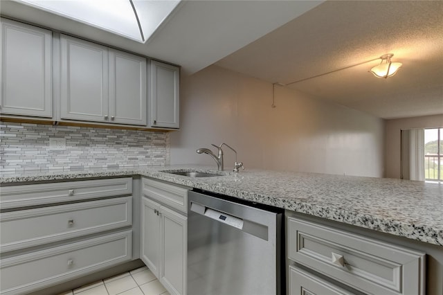 kitchen with backsplash, light stone counters, stainless steel dishwasher, sink, and light tile patterned floors