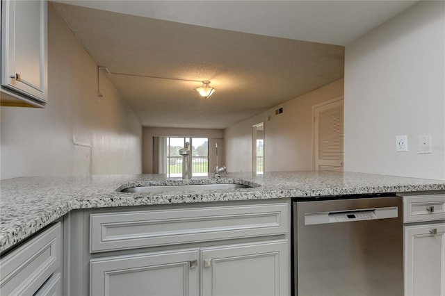 kitchen with white cabinetry, sink, light stone counters, stainless steel dishwasher, and kitchen peninsula