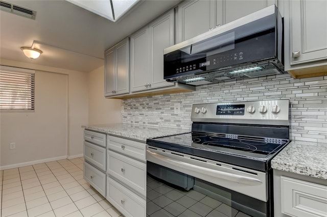 kitchen with electric range, light tile patterned floors, light stone counters, backsplash, and white cabinets