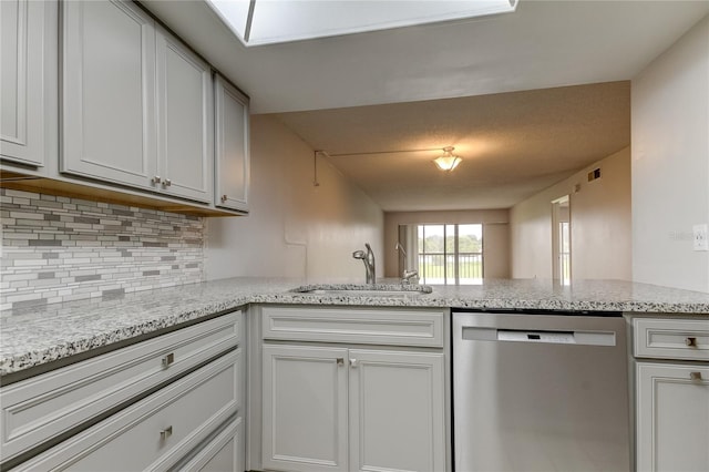 kitchen with kitchen peninsula, light stone counters, stainless steel dishwasher, sink, and white cabinetry